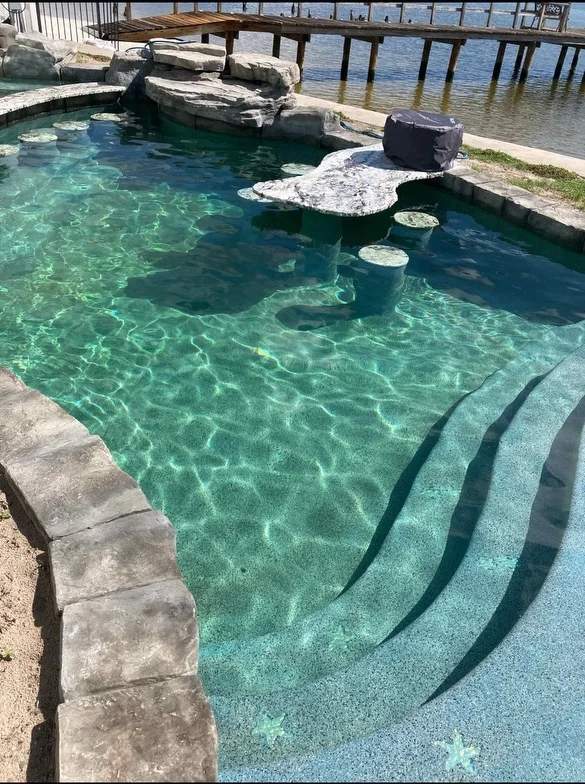 Custom built-in pool table seating detail showing a submerged concrete dining table inside clear turquoise water