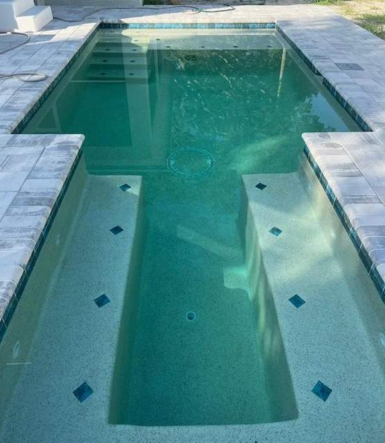 Completed geometric concrete pool featuring double tanning shelves and grey pavers