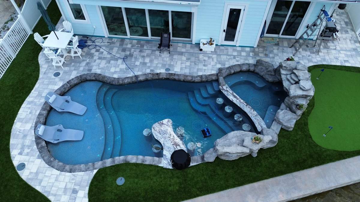 Vertical drone shot of waterfront pool, raised spa, artificial turf, and dock