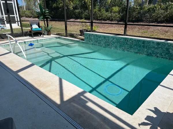 Custom concrete pool inside screen enclosure with green-turquoise mosaic tiles