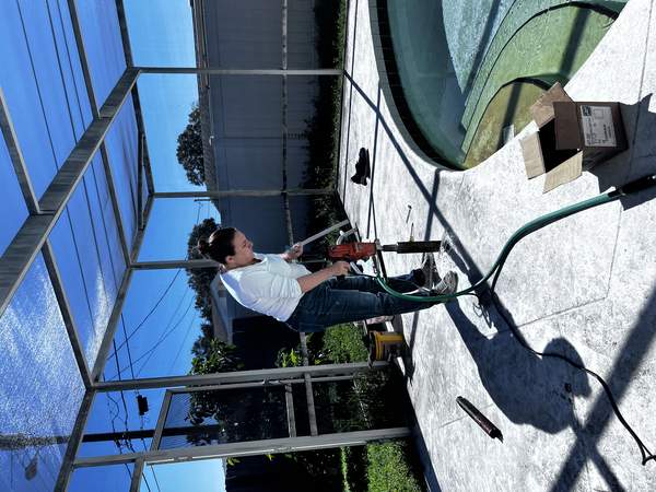 Ada Neikens operating a concrete core drilling machine on a pool deck under a screen