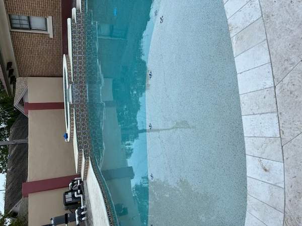 Curved residential pool with raised spa, travertine pavers, and clean equipment set