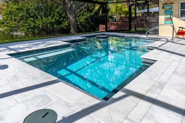 Finished rectangular swimming pool with light travertine pavers overlooking a lake