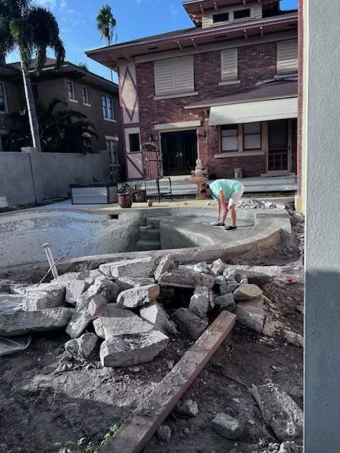 Worker finishing concrete shell steps on a renovation site with debris in foreground