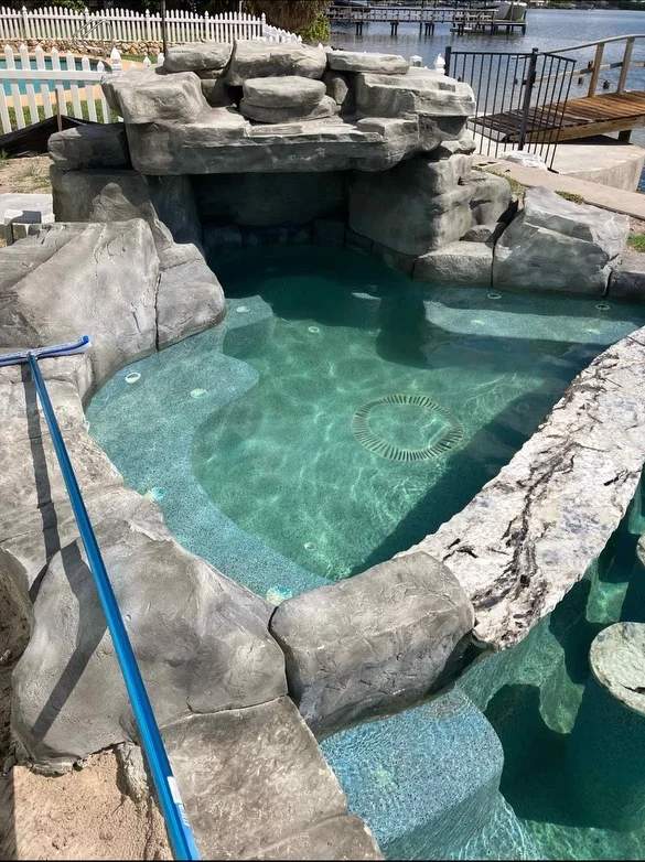 Elevated rock waterfall spa spilling into the main pool waterway next to a dock